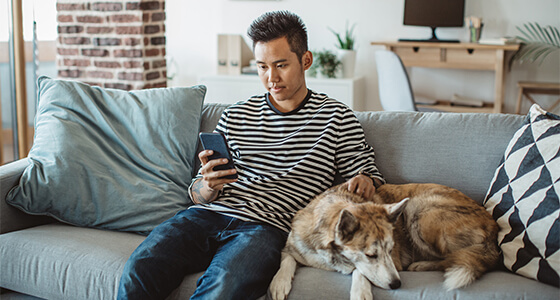 Man on the couch with dog while reading his phone